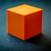 Close-up of an orange foam cube on a dark surface, highlighting its texture and color contrast.